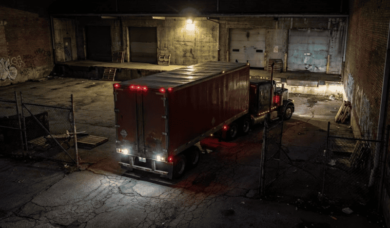Semi truck and trailer at night in a shady area.